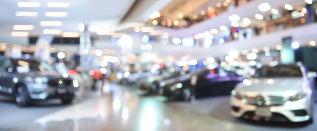 A blurred image of a car dealership showroom with cars on display. 