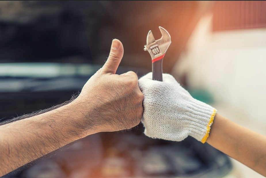 Mechanic giving a thumbs up while holding an adjustable wrench during auto service.